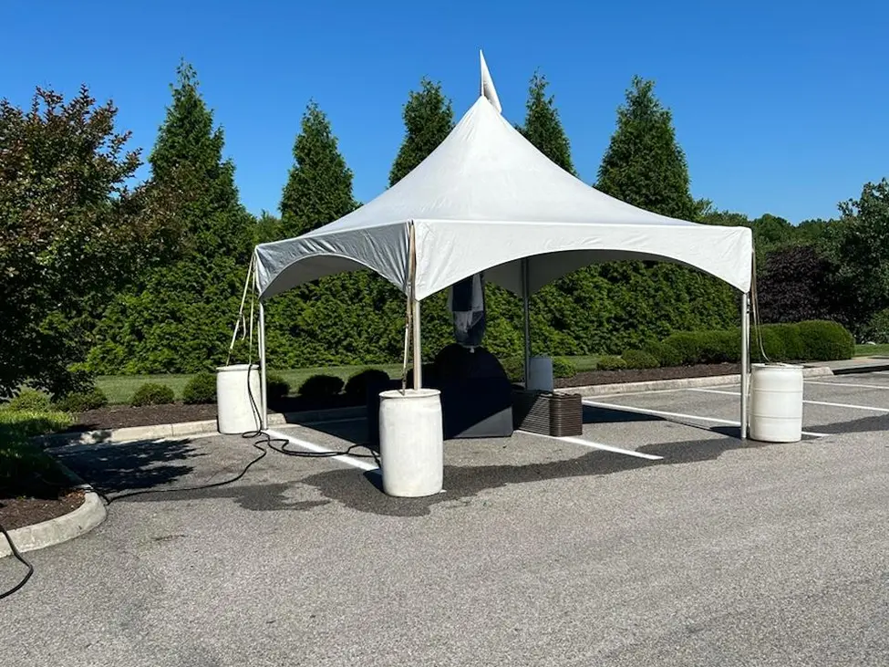 White canopy tent set up outdoors on a paved area with trees in the background.