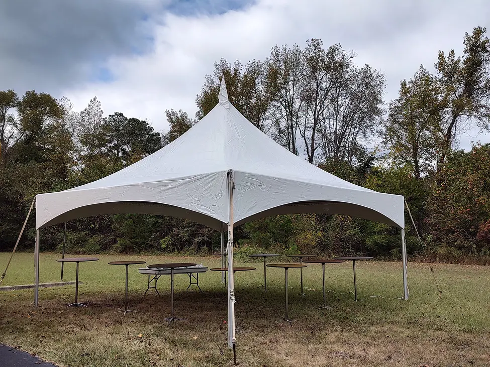White canopy tent set up in a grassy field with trees in the background.