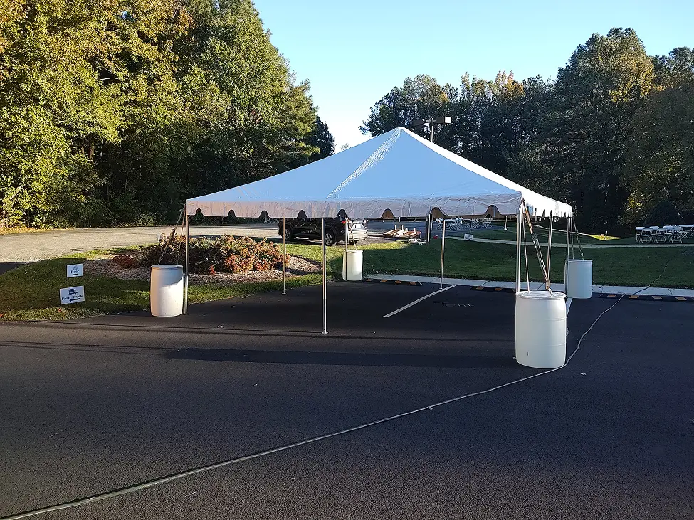 Empty white event tent set up in a parking lot with trees in background.