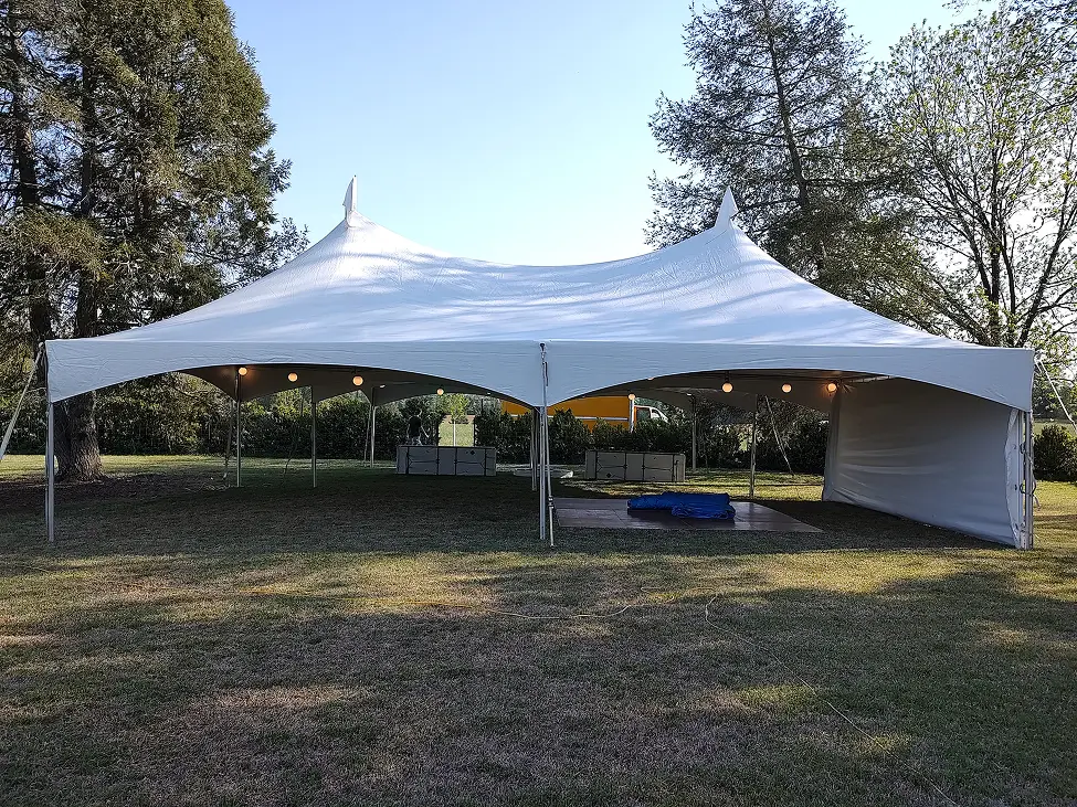 Large white event tent set up outdoors on grass under trees.