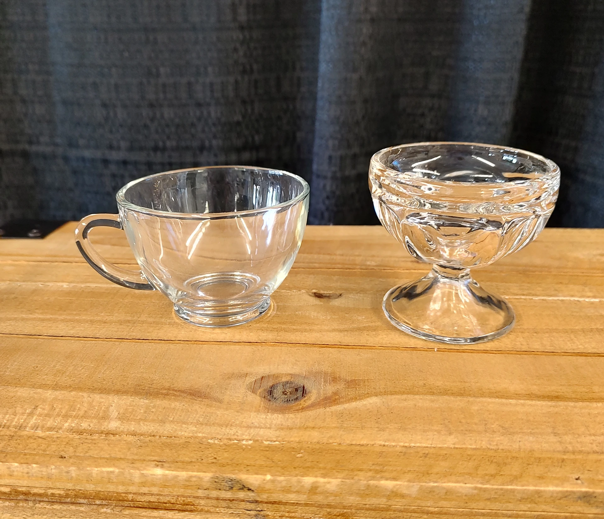 Two empty glass cups on a wooden surface against a dark background.