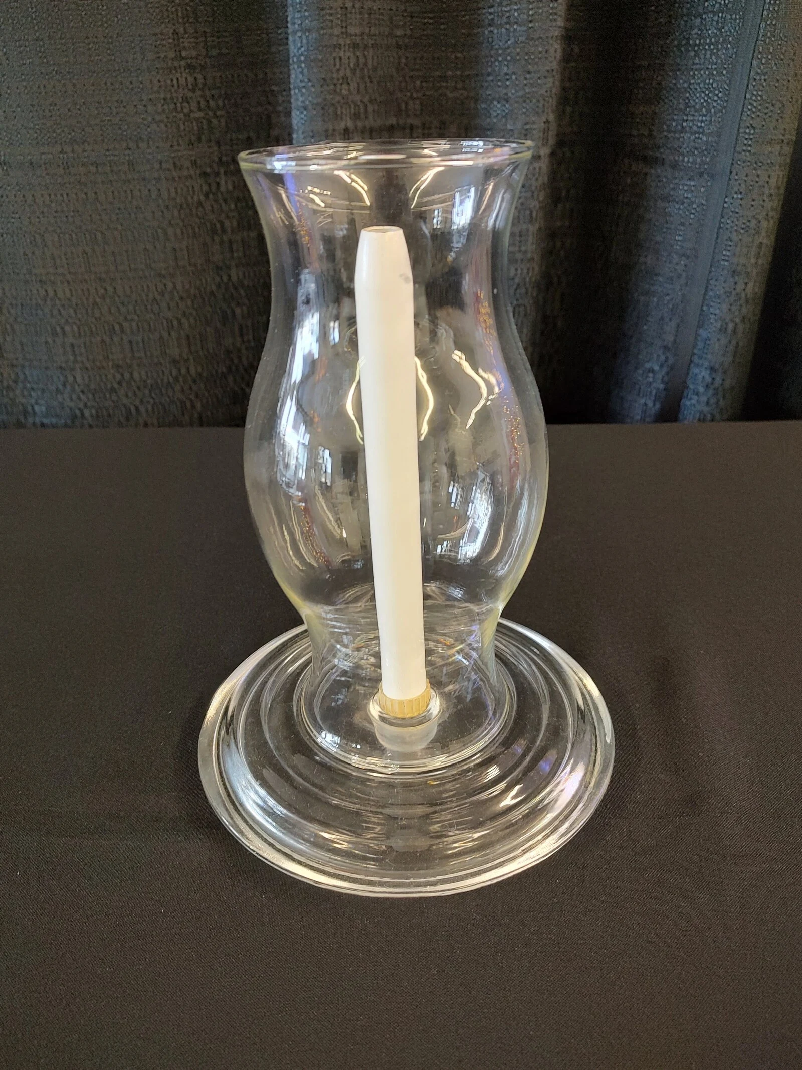 A clear glass hurricane candle holder with a white candle inside.