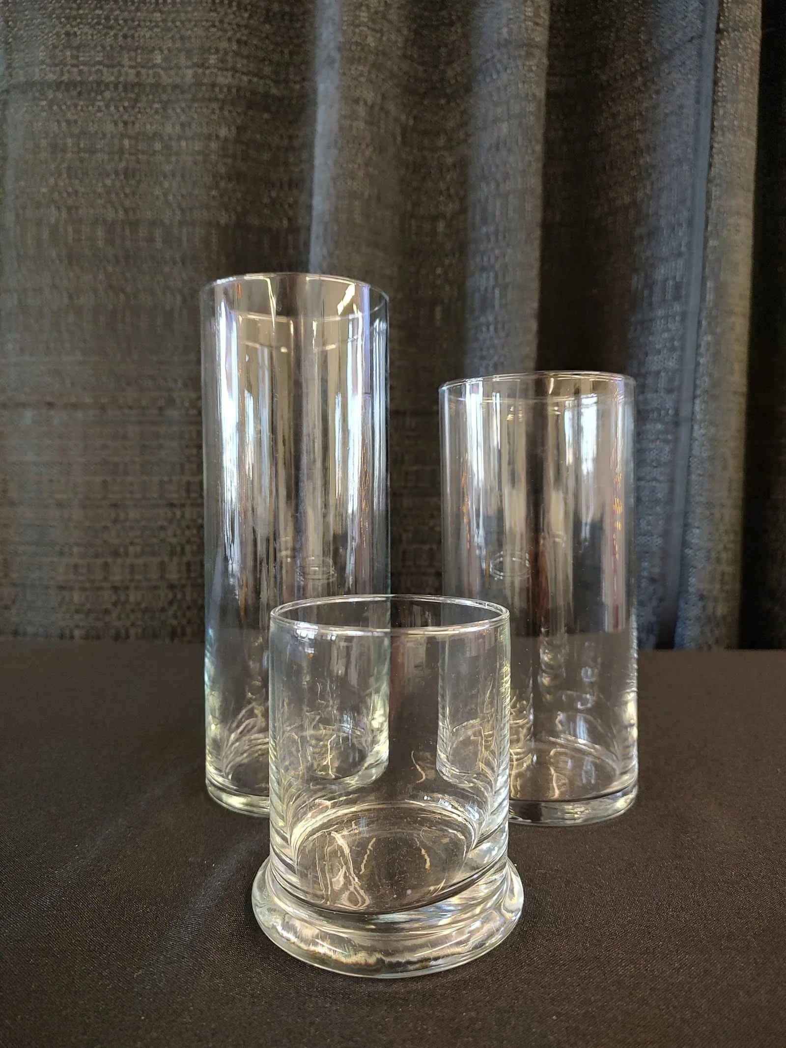 Three clear glass cylindrical vases of varying heights on a surface.