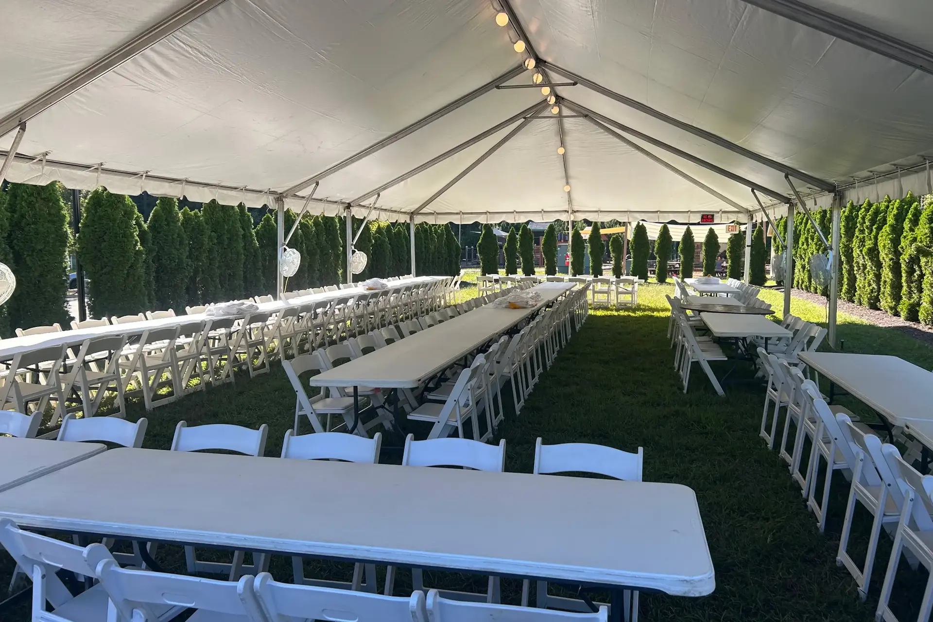 Long tables with white chairs set under a large tent for an outdoor event.