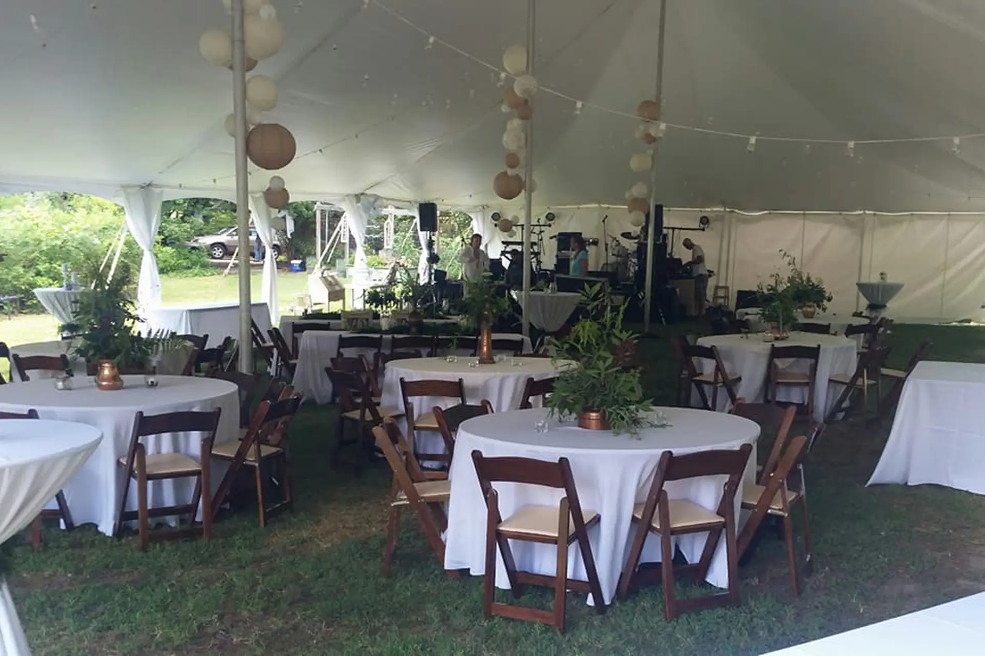 A tented outdoor event setup with round tables and wooden chairs.